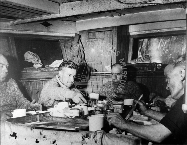 Fishermen having meal in cabin of trawler, c.1950.