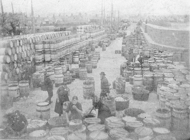 Fisherlasses and barrels on pier.